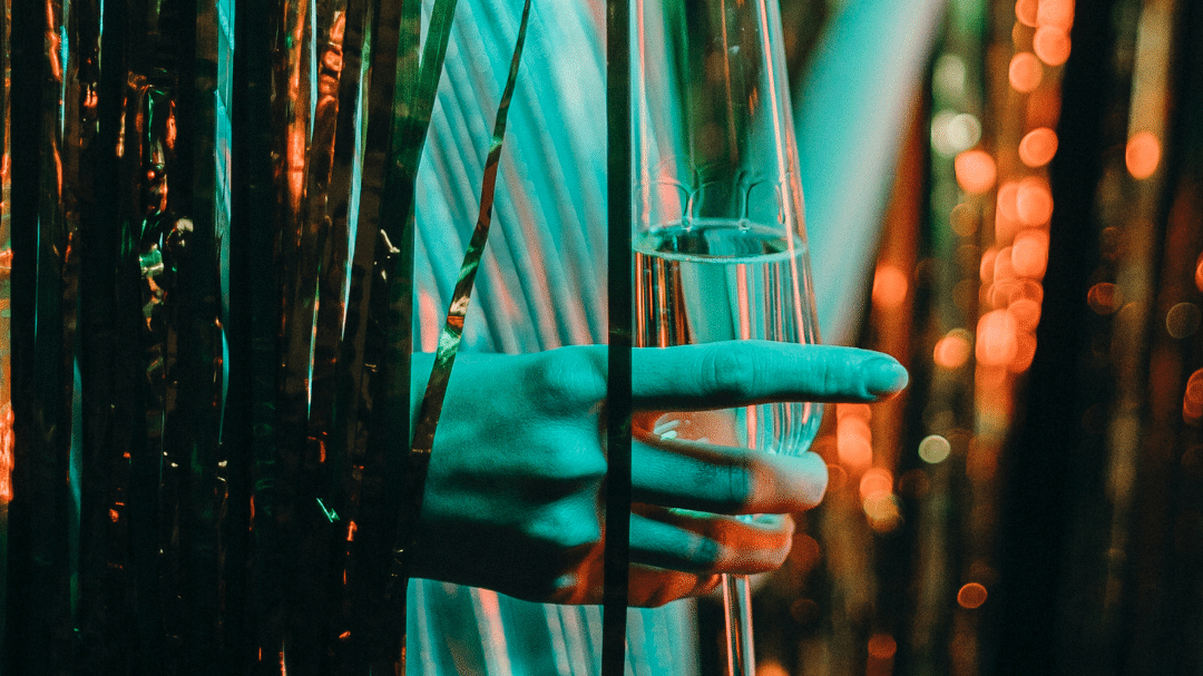 uma mão segurando uma taça de champanhe entre cortinas metalizadas douradas