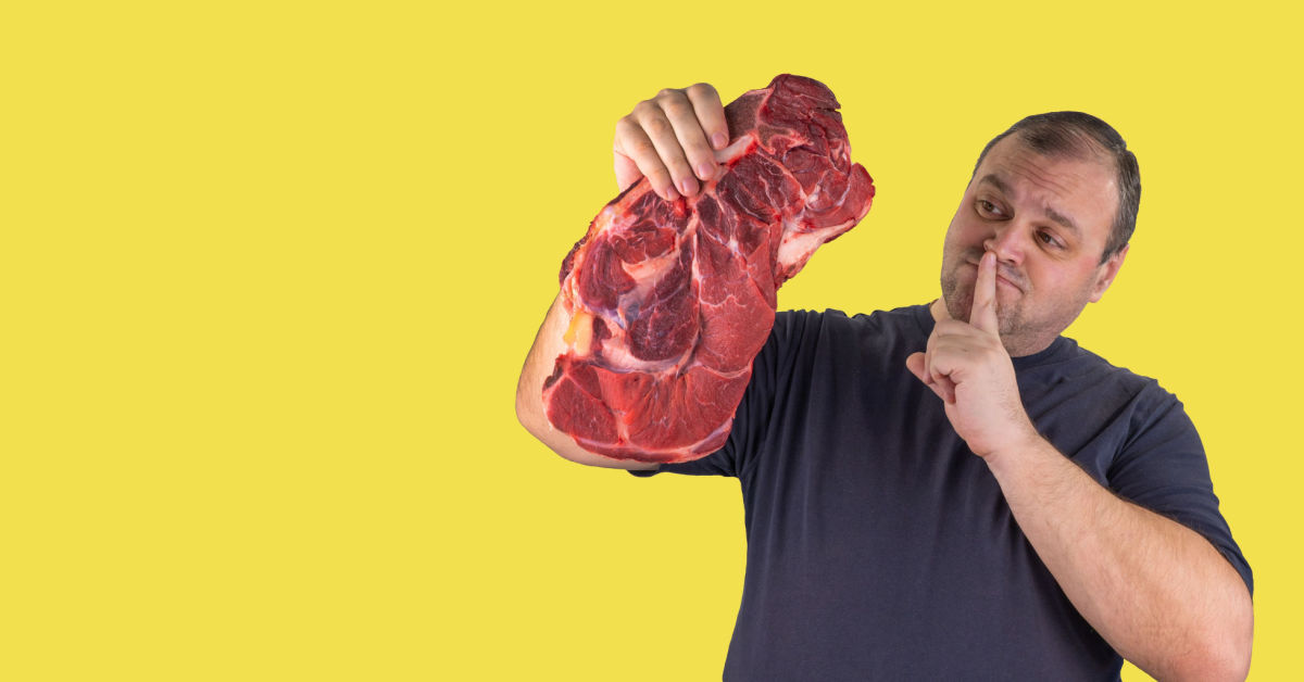 Homem segurando um pedaço de carne e fazendo sinal de silêncio