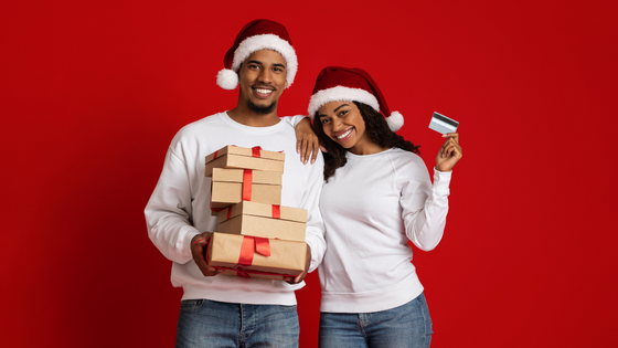 Casal negro usando gorro de Papai Noel, segurando caixas de presente e cartão de crédito