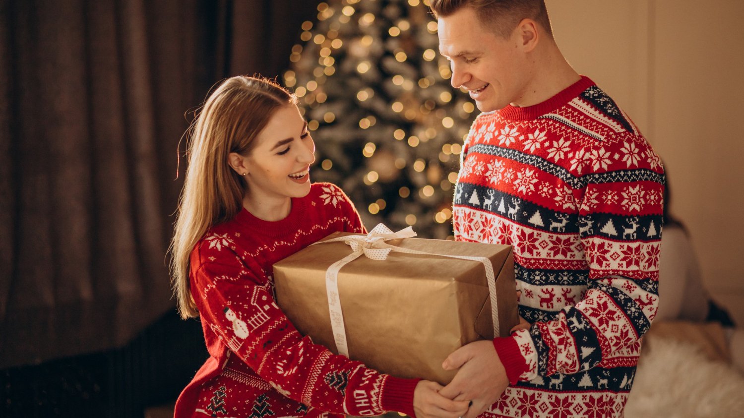 Casal segurando caixa de presente usando roupas temáticas do natal