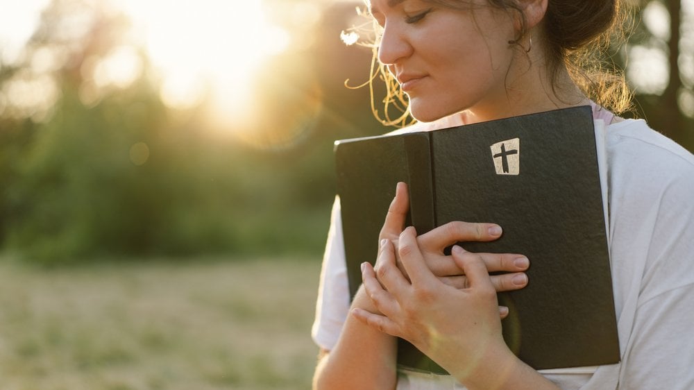 Mulher segurando a Bíblia com ar de serenidade, em dia de sol