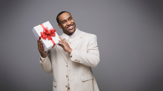 Homem usando terno e sorrindo, enquanto segura uma caixa de presentes.