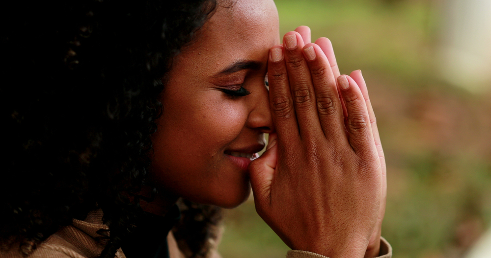 Mulher com os olhos fechados e as mãos dadas na frente do rosto, orando