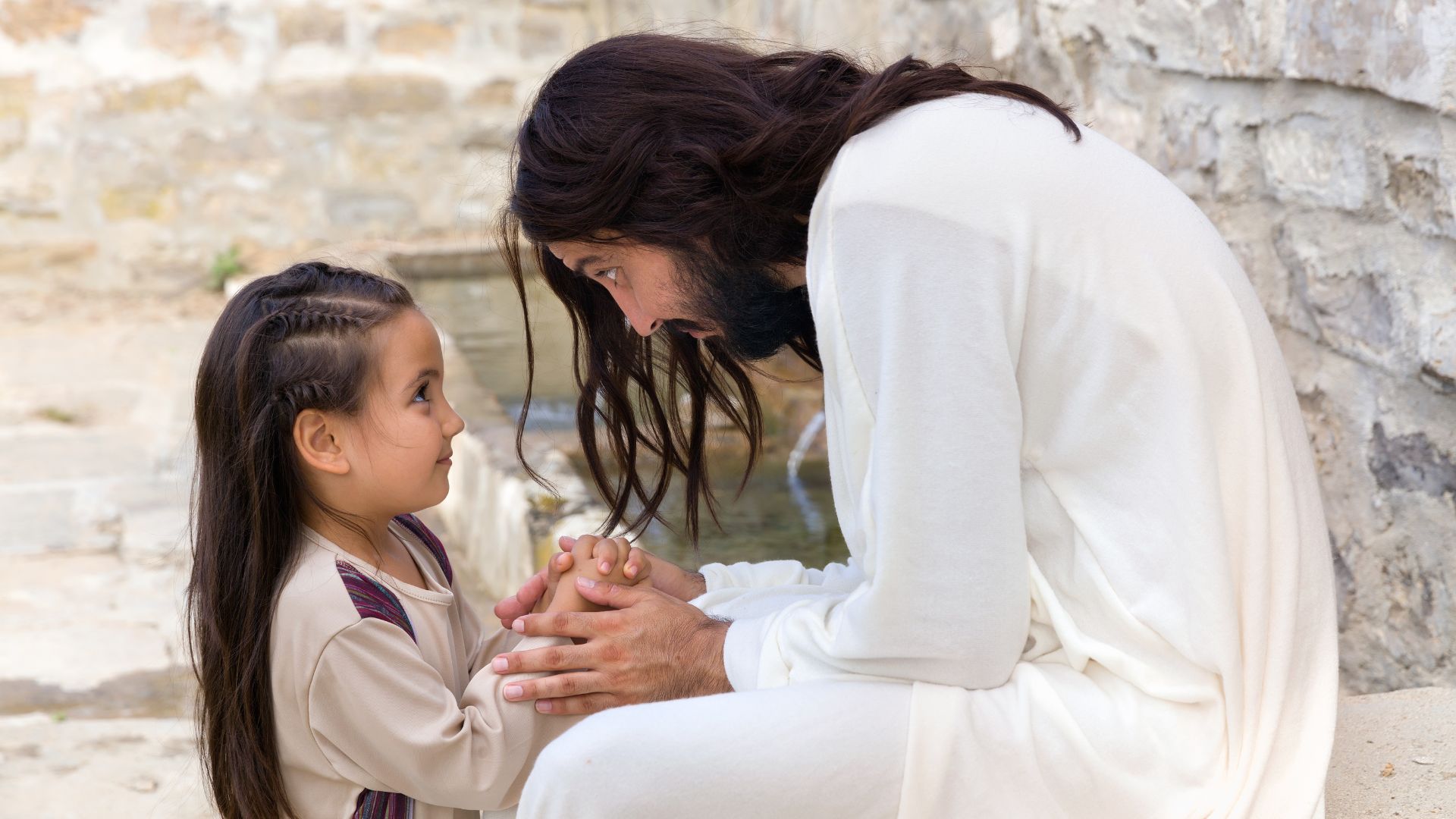 Imagem de um homem representando Jesus falando com uma garotinha que está sorrindo