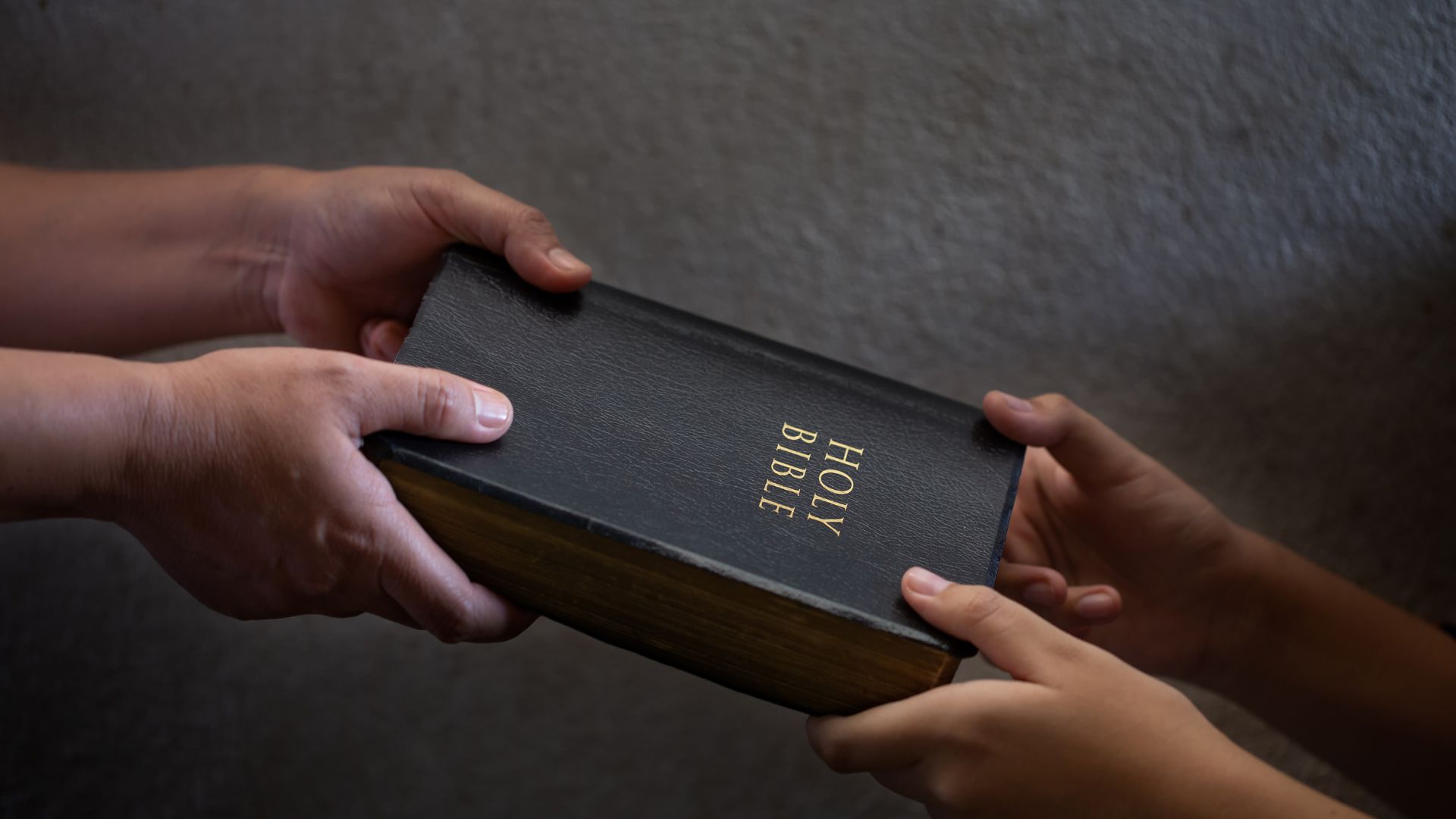 Imagem só das mãos de uma pessoa entregando uma Bíblia para a outra.