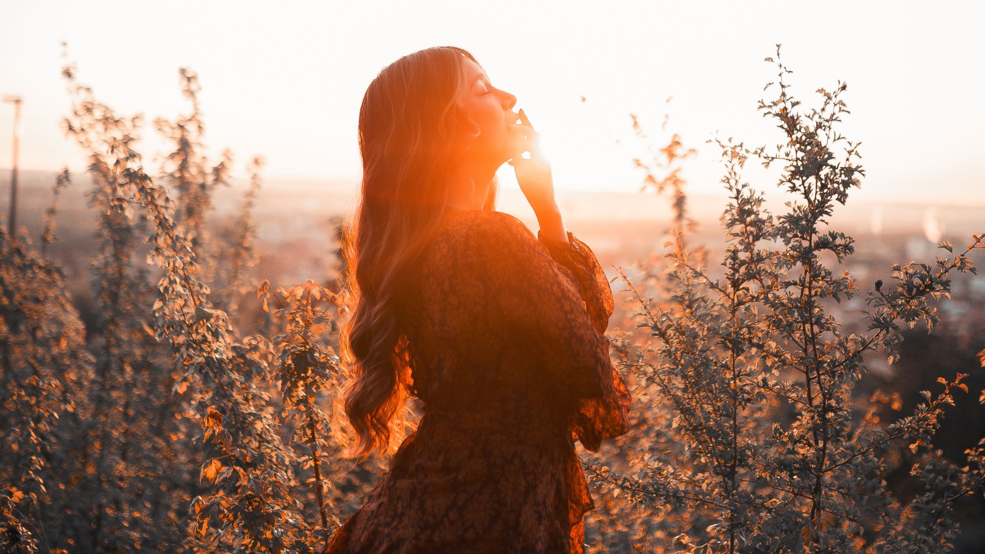 Imagem de uma mulher no meio de um campo olhando para cima e o por do sol atrás dela