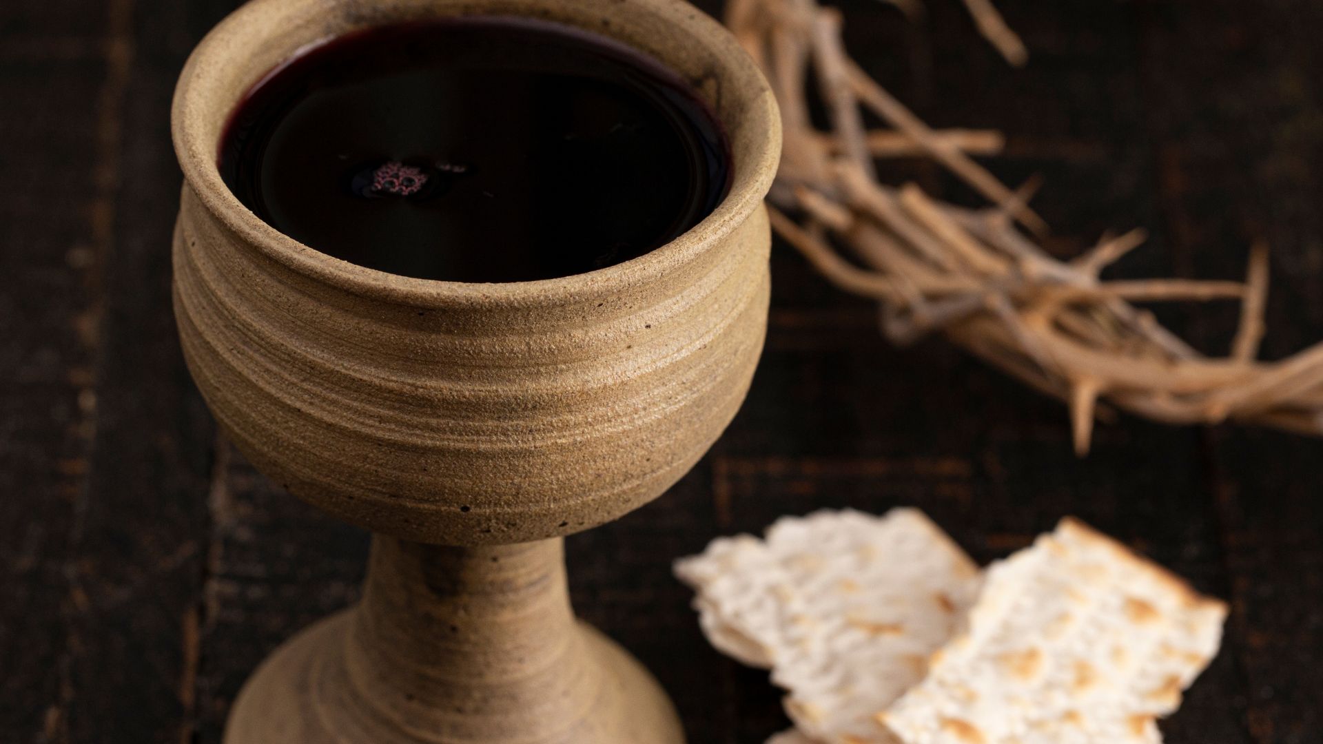 Imagem de uma taça de vinho, pães ázimos e uma coroa de espinhos do lado como representação da ceia de Jesus