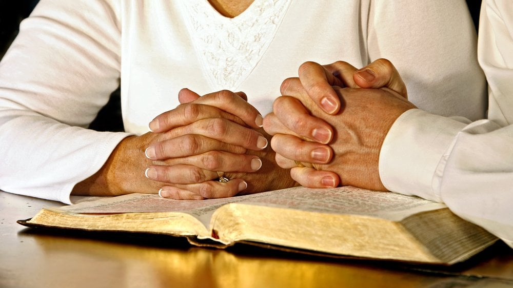 Casal com as mãos em cima de uma Bíblia, orando