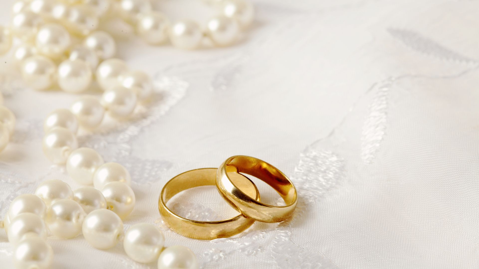 Foto de duas alianças de casamento em um tecido branco com pérolas