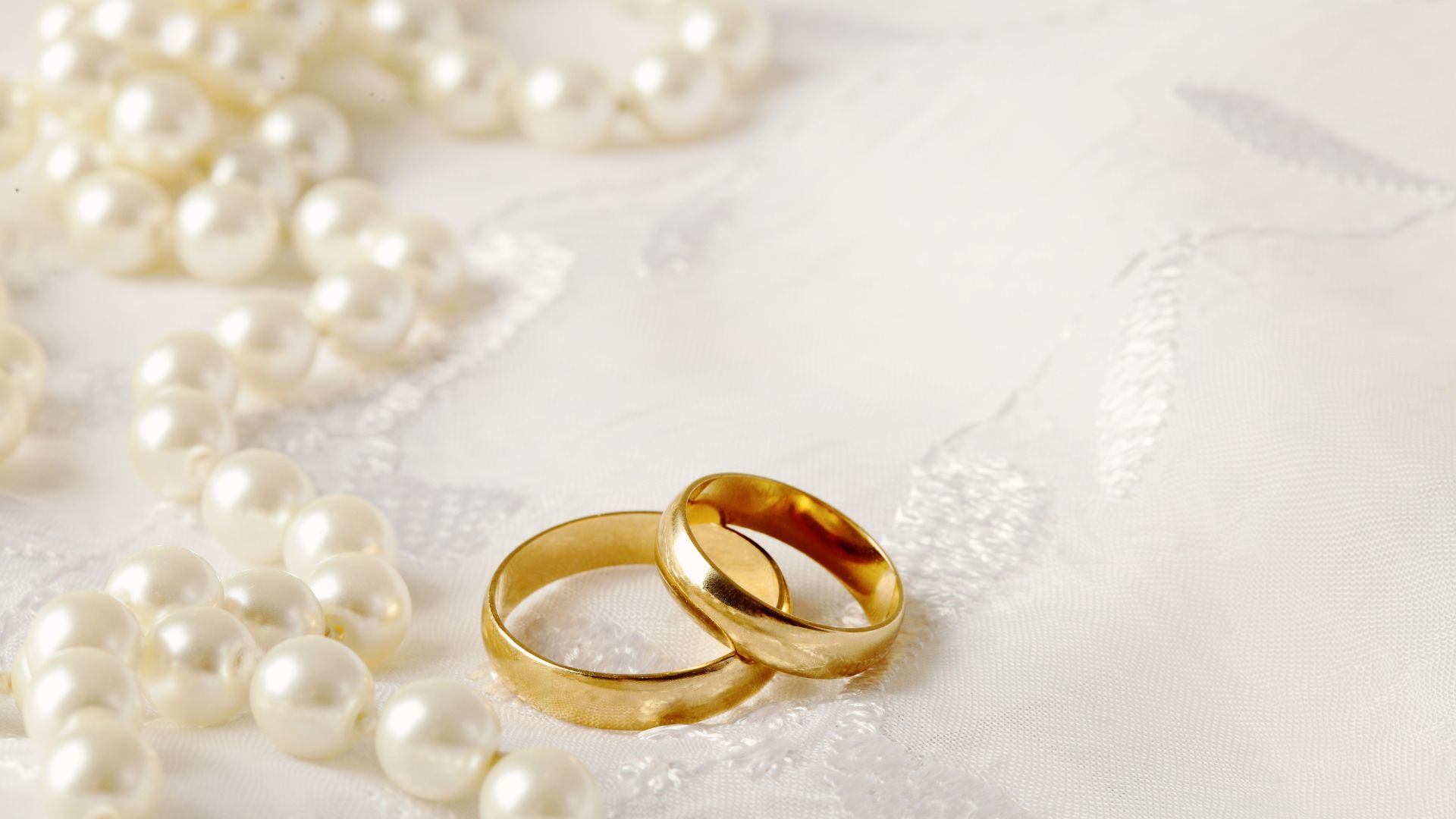 Mensagens Com Amor/ Canva/ KMNPhoto de Getty Images Pro Foto de duas alianças de casamento em um tecido branco com pérolas