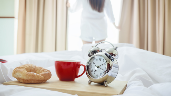 Café da manhã na cama e ao fundo, uma mulher olhando pela janela