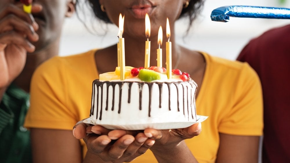 Mulher segurando um bolo de aniversário com as duas mãos e assoprando as velas