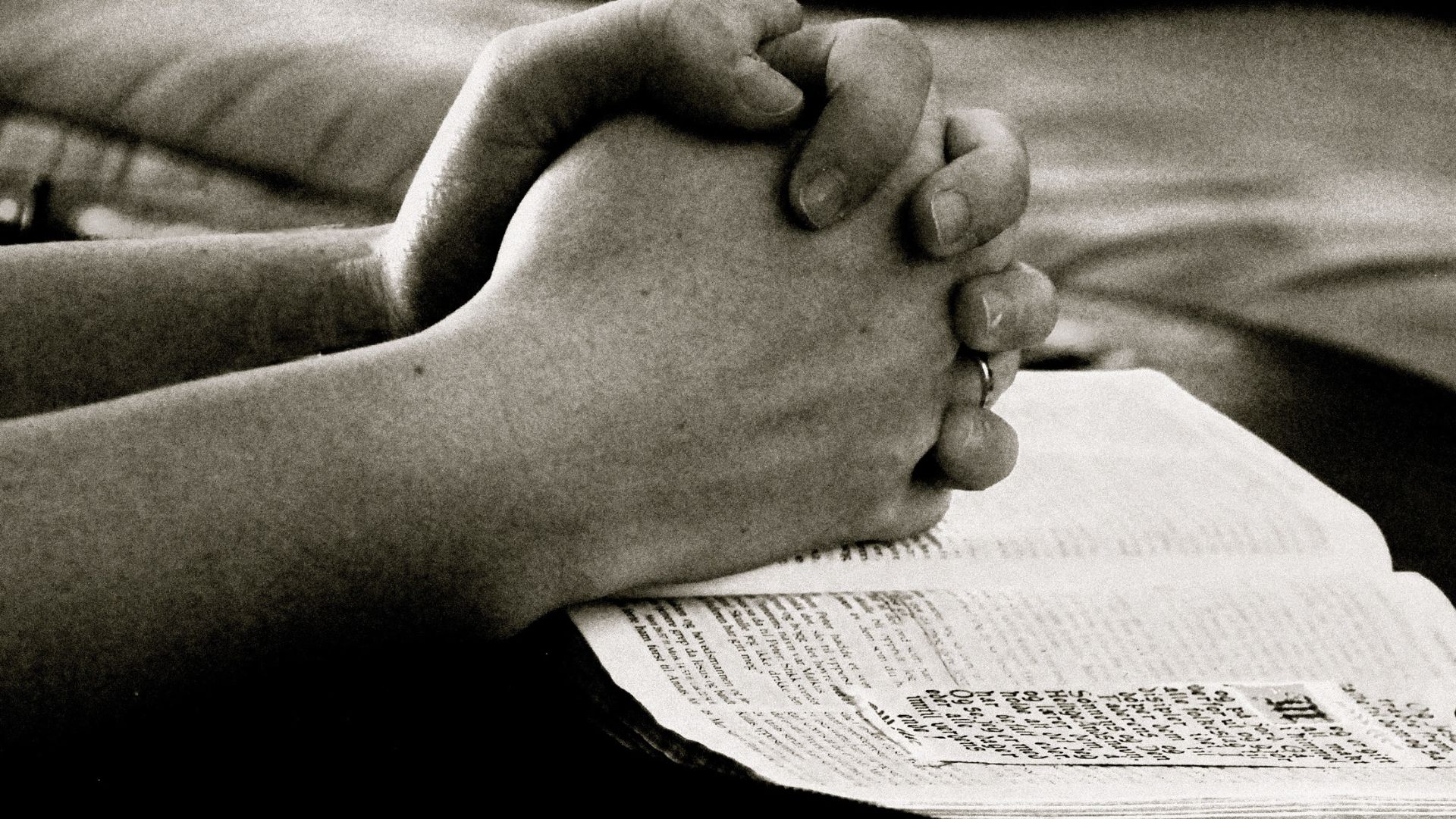 Imagem das mãos de uma pessoa em posição de oração em cima de uma Bíblia