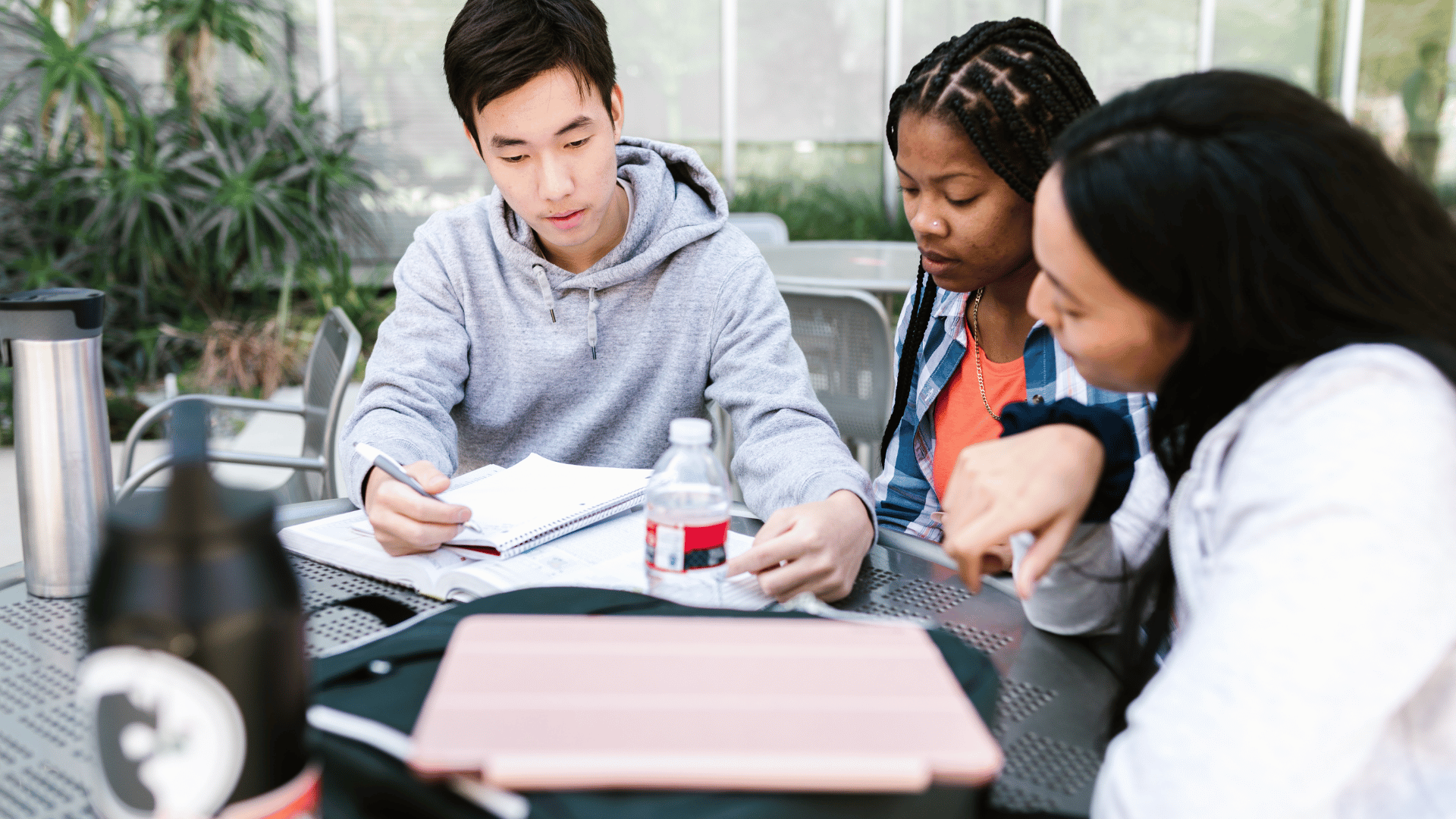 Três jovens estudando juntos em uma mesa redonda.