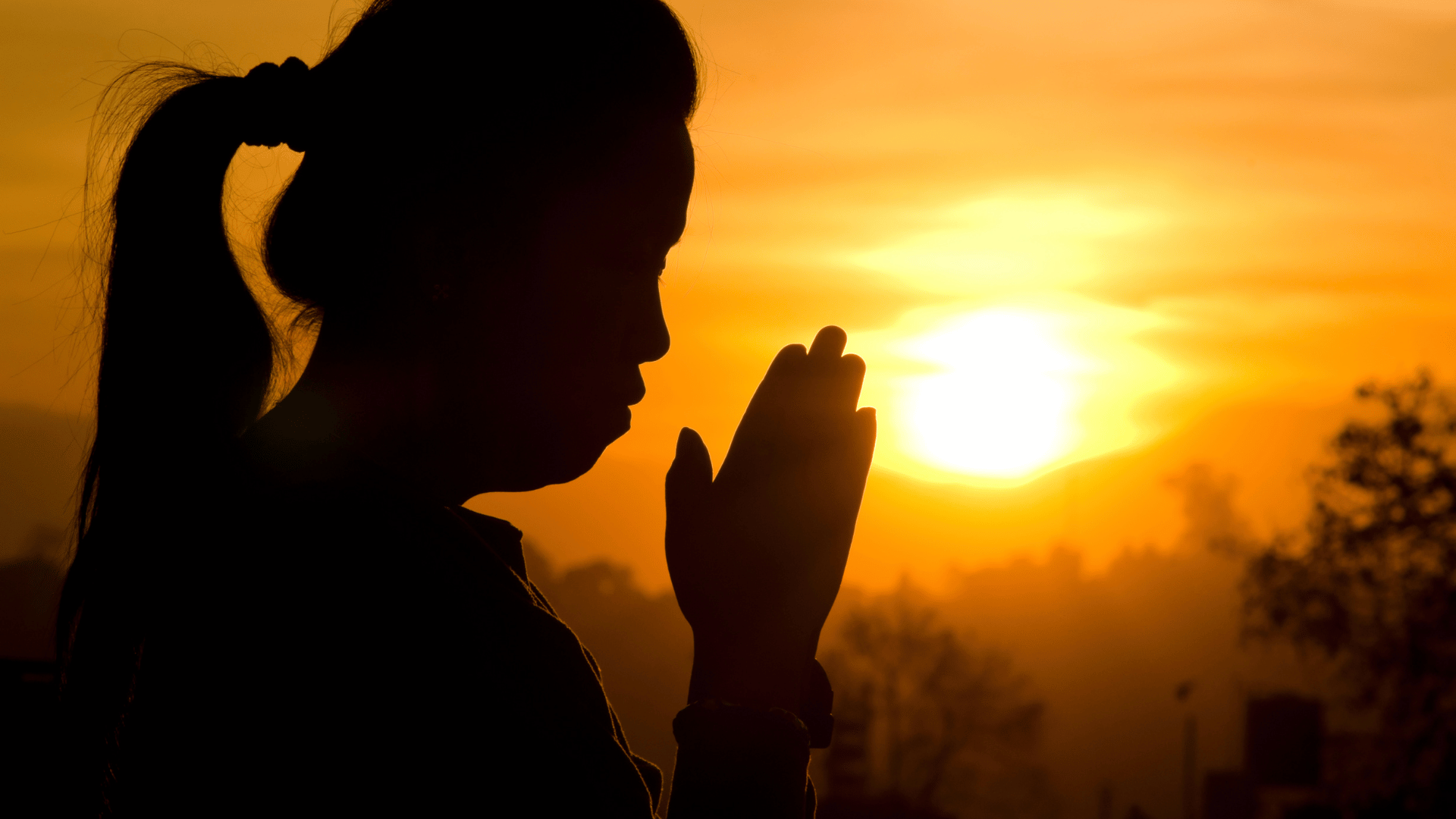 Mulher ao entardecer juntando as mãos em sinal de gratidão.