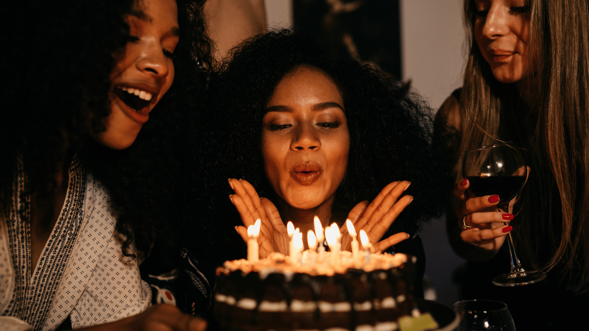 Mulher assoprando as velas do seu bolo de aniversário ao lado das amigas