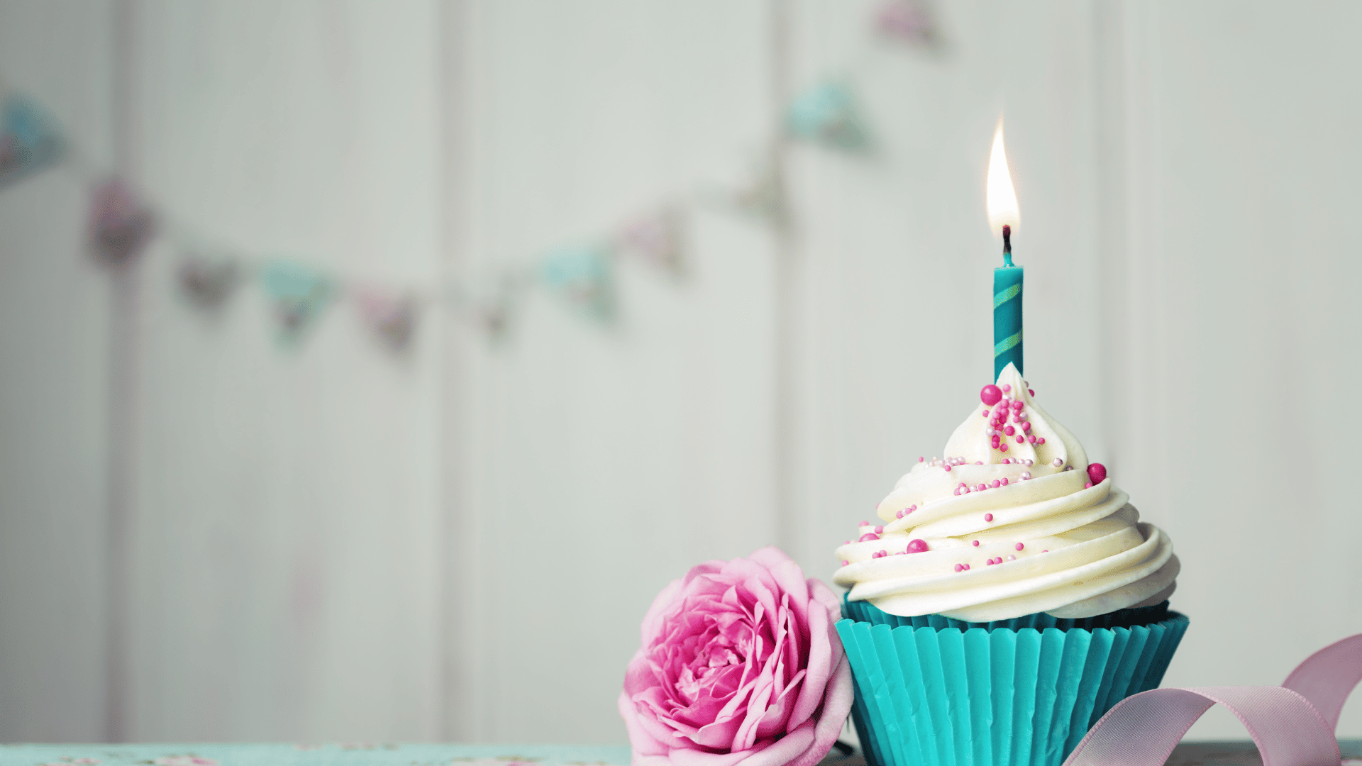 Cupcake com uma vela azul em um cenário de festa com uma rosa ao lado.