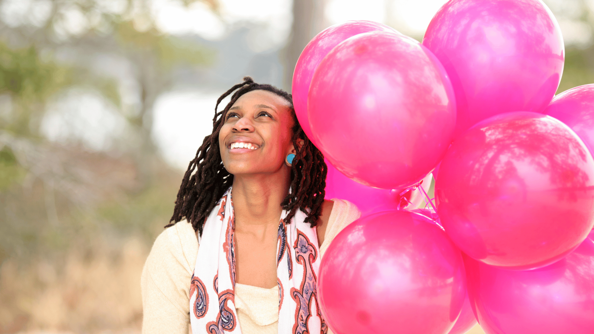 Mulher negra sorrindo segurando balões rosa em seu aniversário.