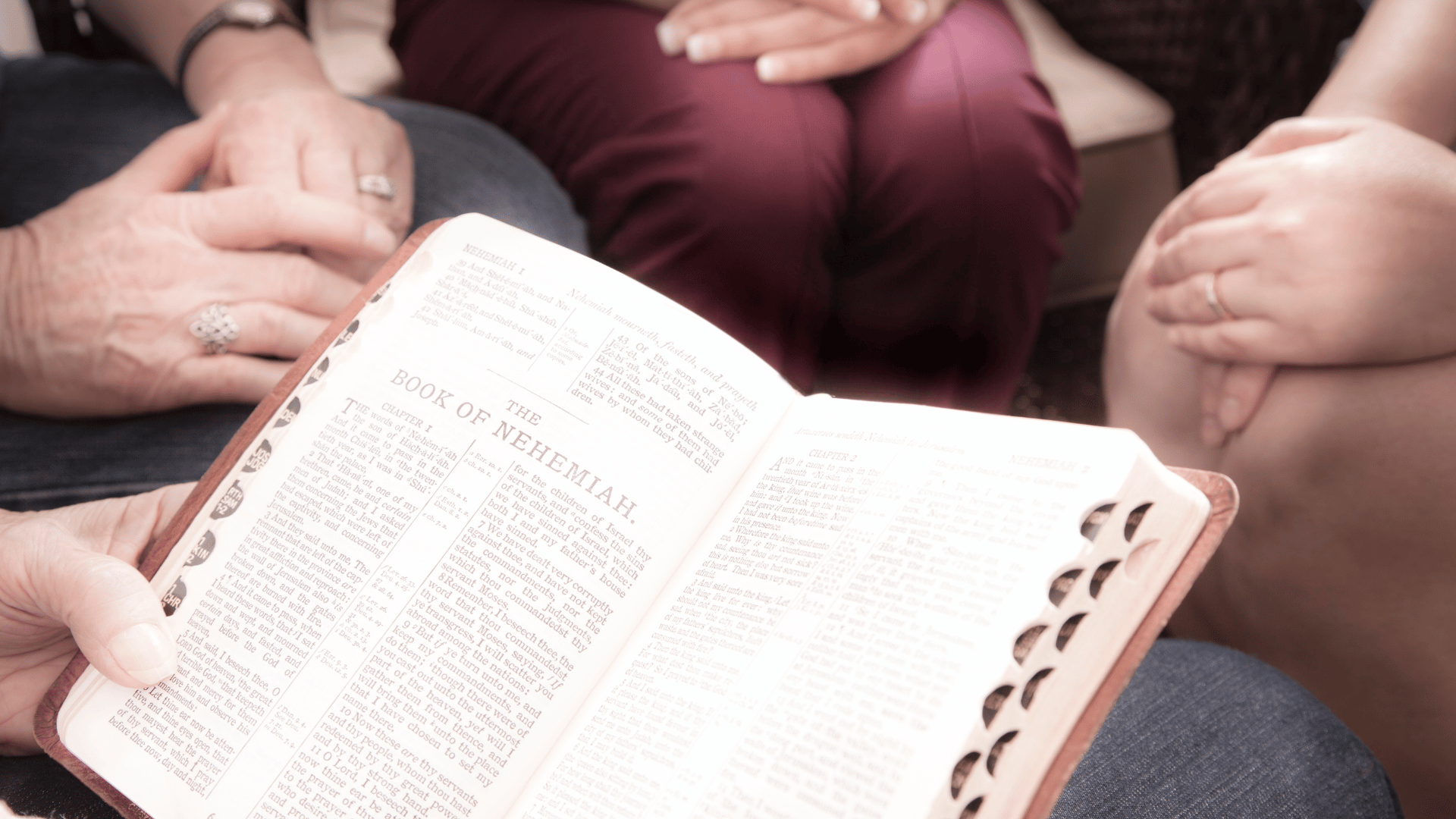 Círculo de pessoas sentadas com as mãos sobre os joelhos em volta de uma pessoa que lê o Livro de Neemias da Bíblia sagrada.