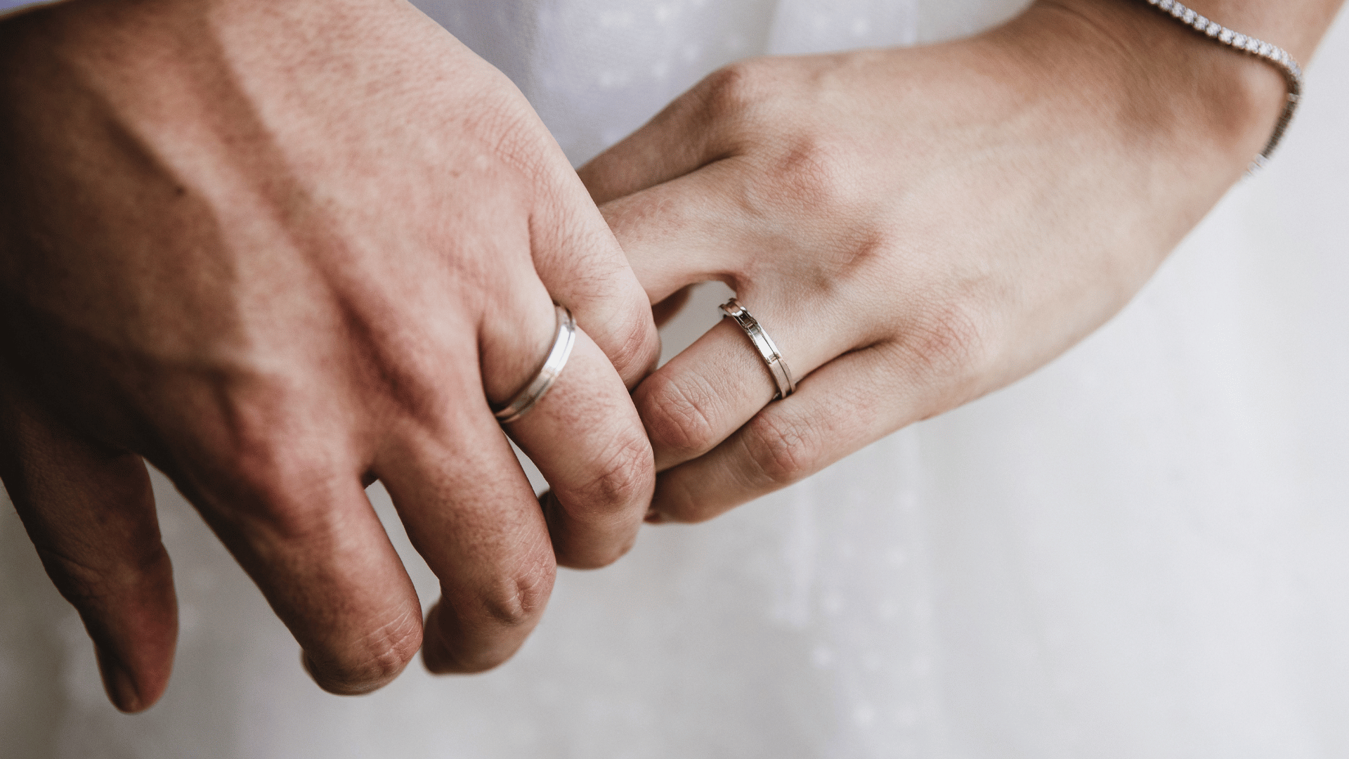 Um homem e uma mulher encostando os dedos anelares com alianças de casamento.