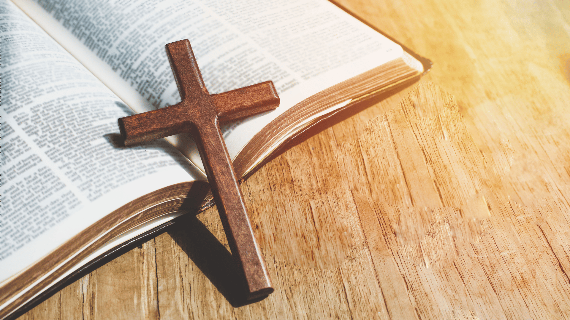 Bíblia aberta em uma mesa de madeira com uma cruz sobre as páginas.