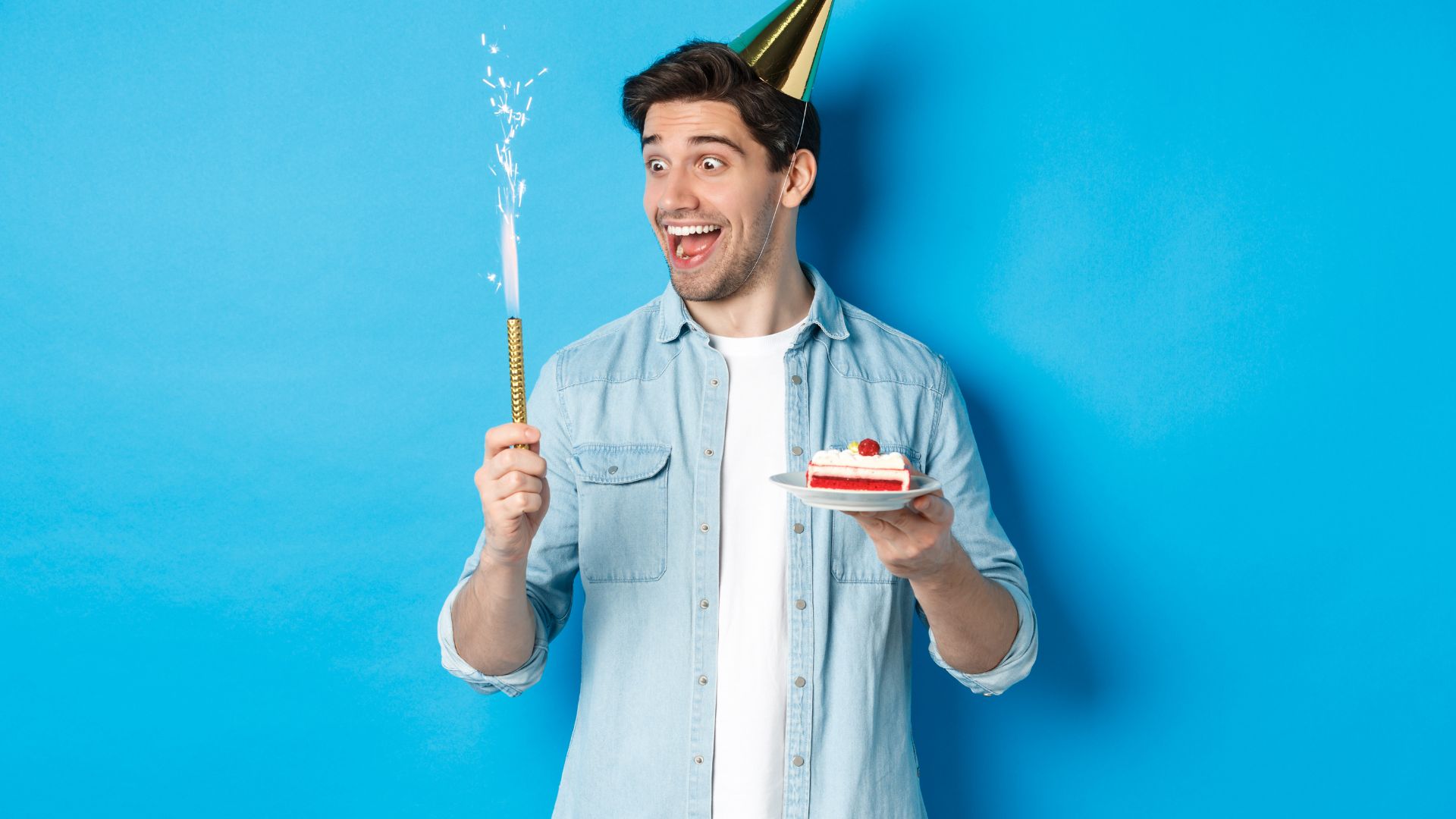 Imagem de um jovem sorrindo e segurando uma fatia de bolo e na outra mão uma vela de aniversário