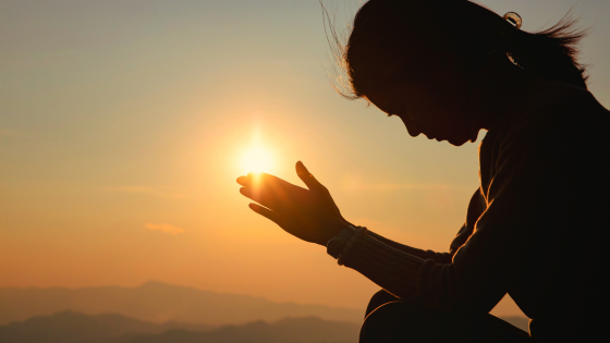 Silhueta de mulher orando sob luz do sol