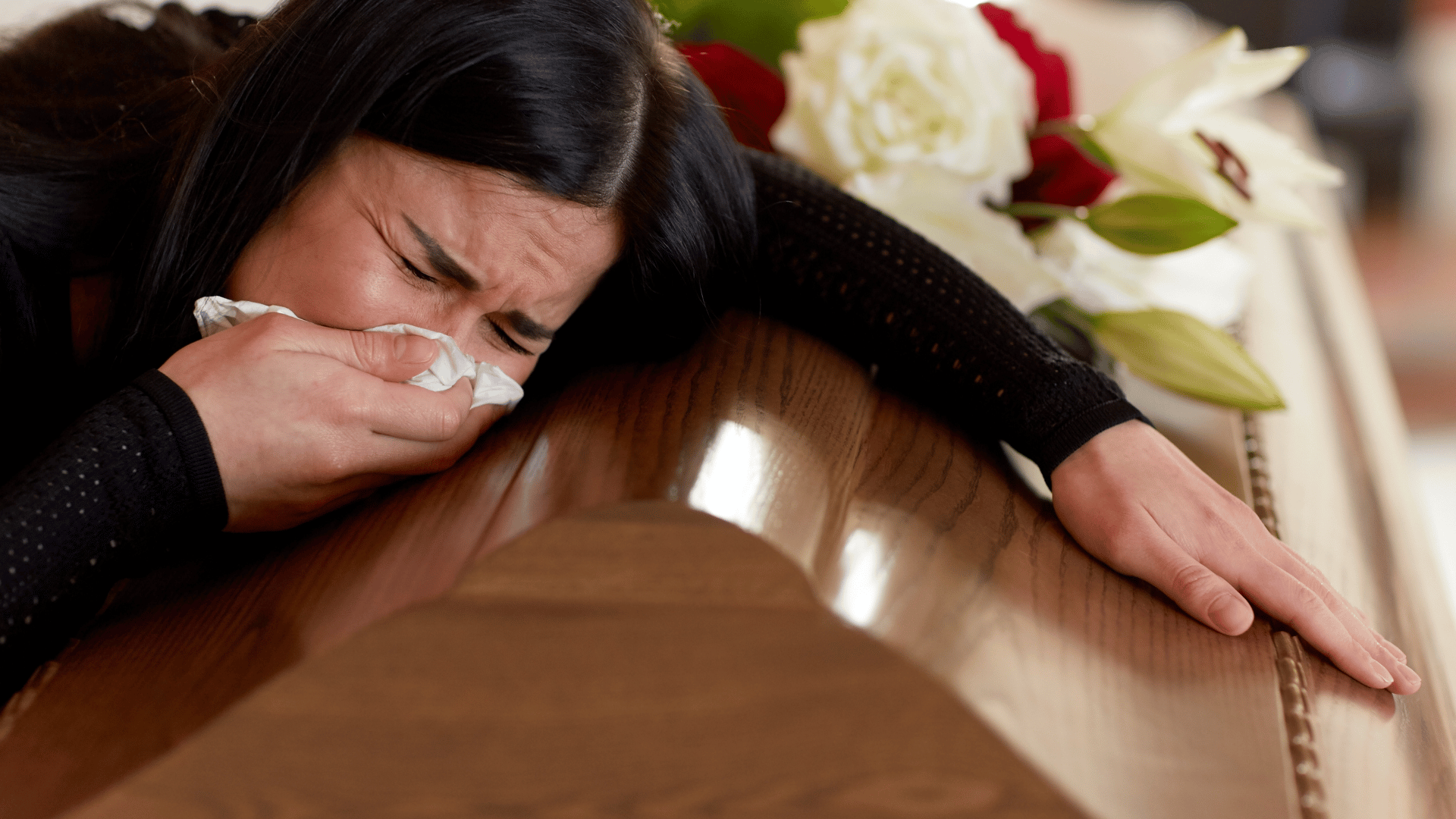 Mulher chorando sob o caixão em um funeral.