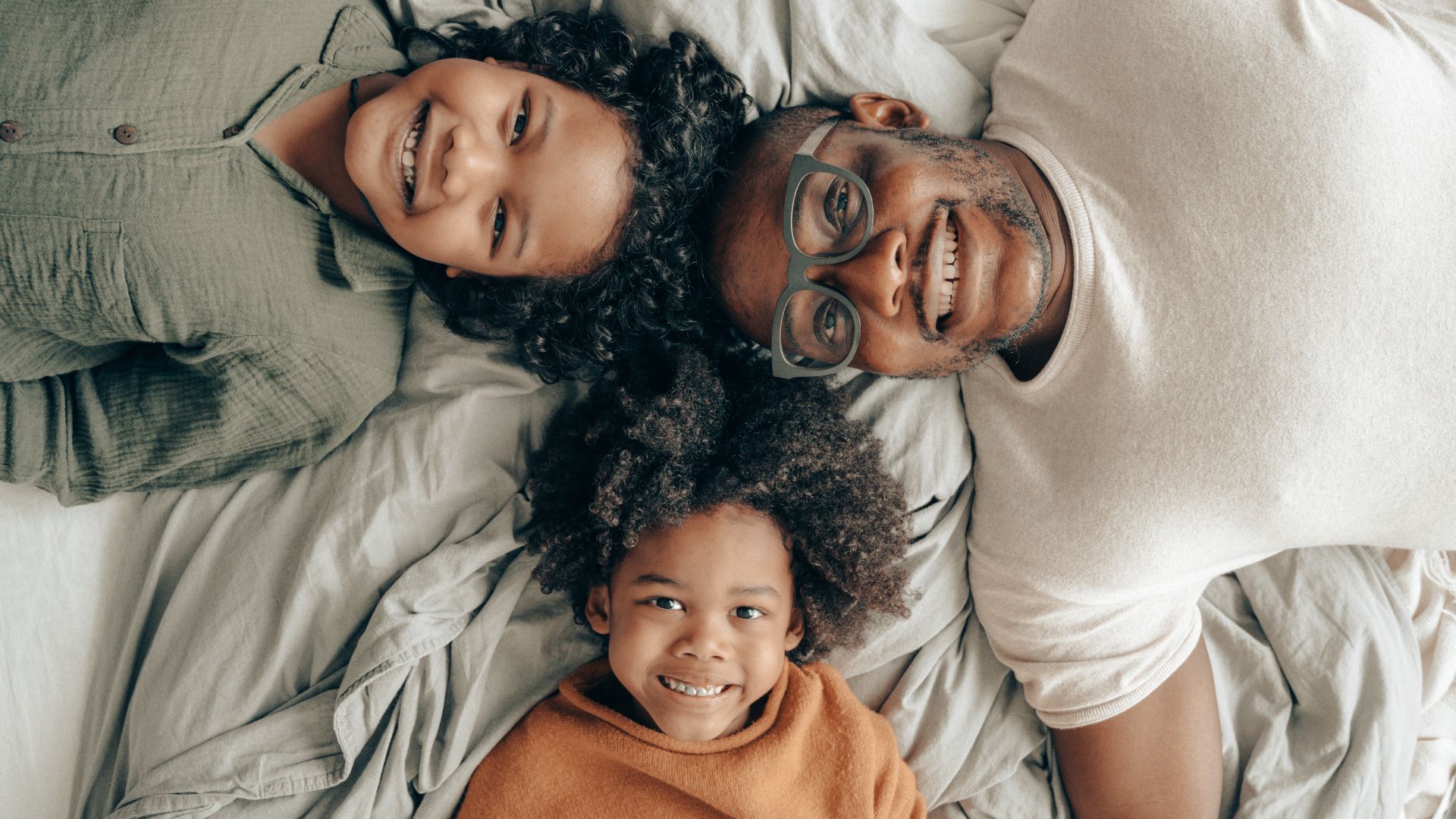 Pai, mãe e filho deitados na cama sorrindo.