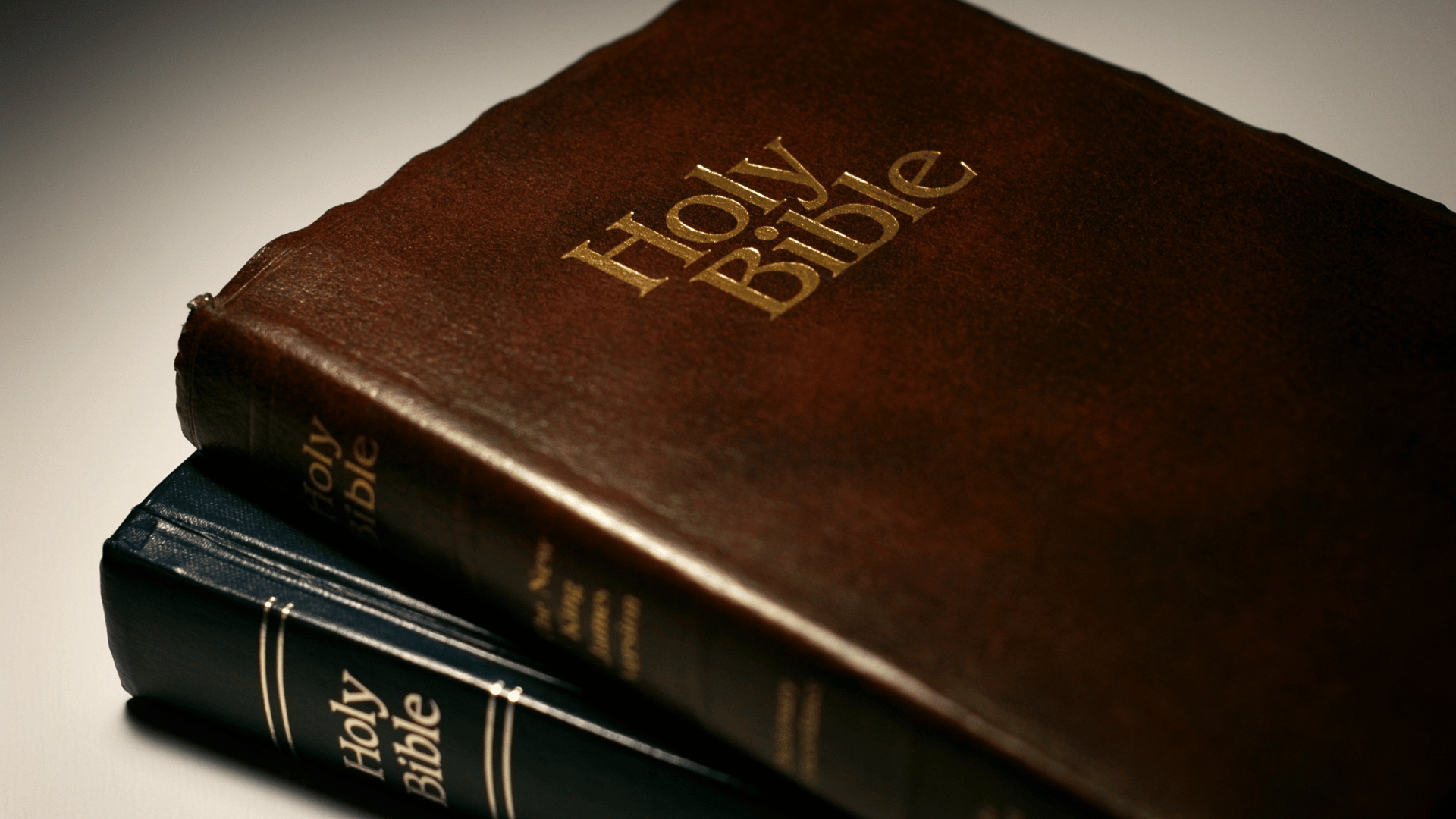 Duas bíblia sagradas, uma sobre a outra. Há um livro em capa dura marrom e outro preto, ambos em couro.