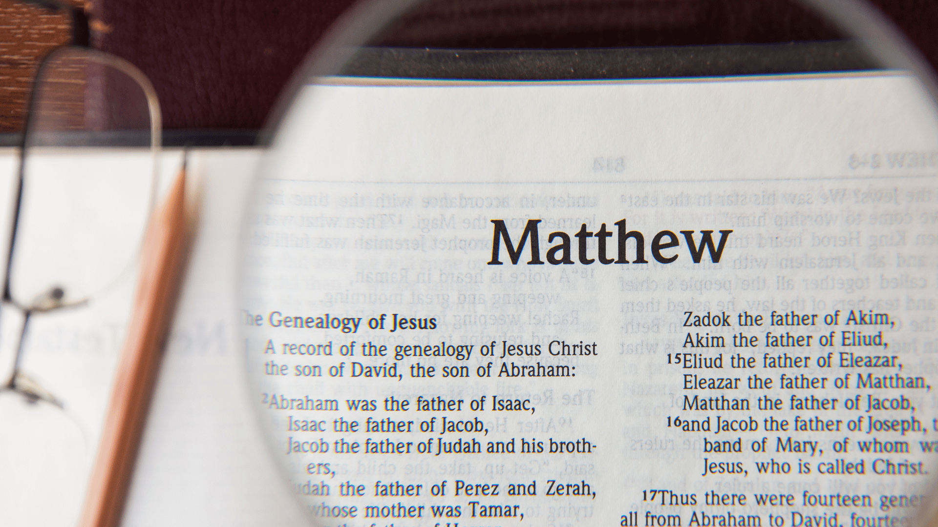 O livro de Mateus. O nome está em zoom por causa de uma lupa, sobre uma mesa com um óculos ao lado.