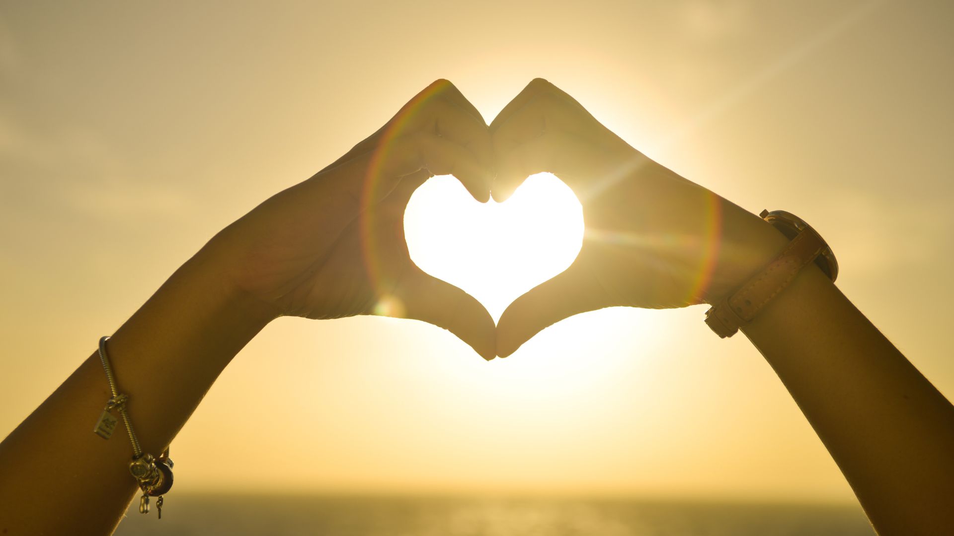 Stokpic de Pexels/ Canva Pro Mãos em formato de coração levantadas para cima, ao ar livre de frente para o sol