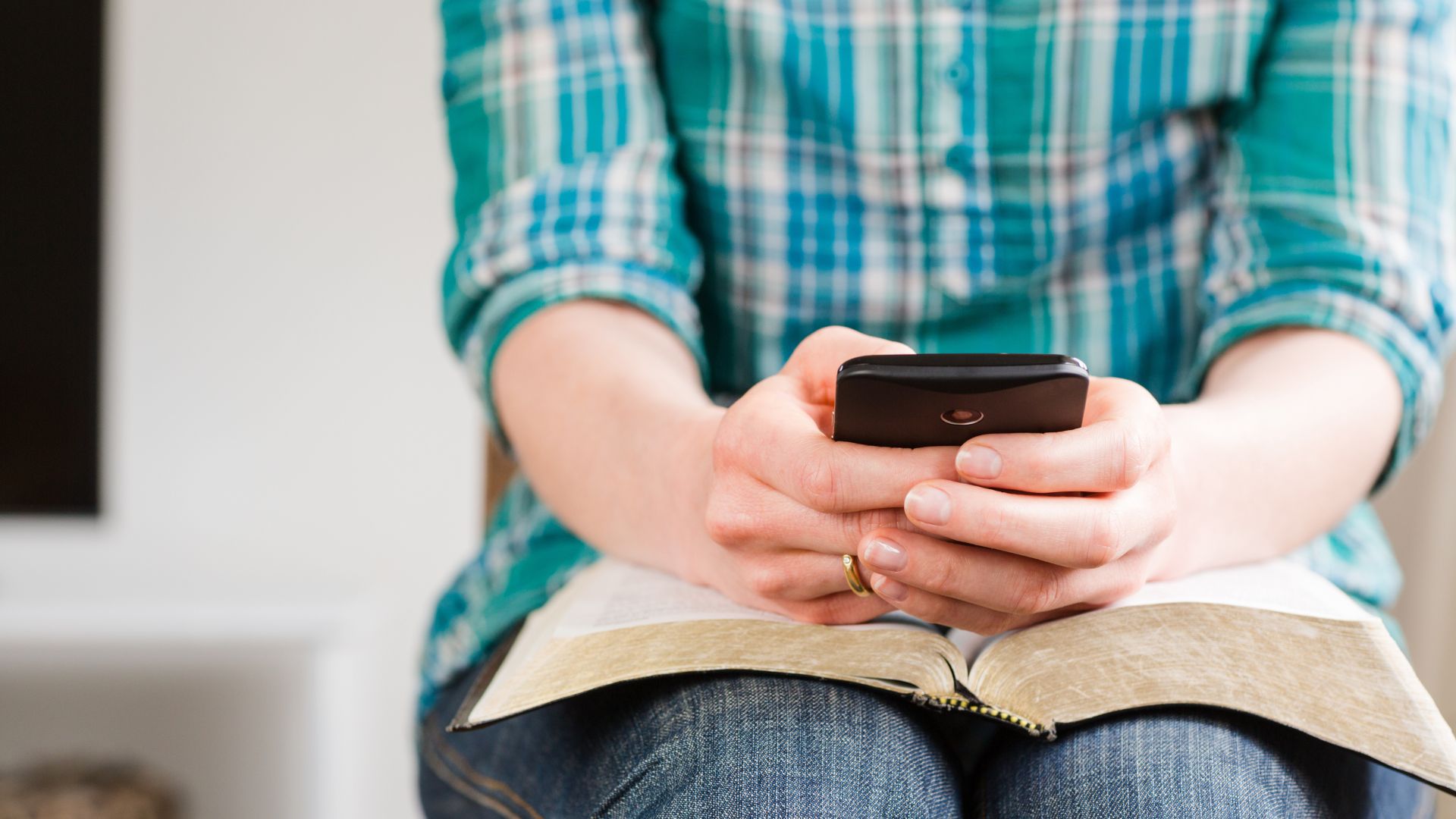 Mulher, sentada com uma Bíblia no colo e um celular na mão