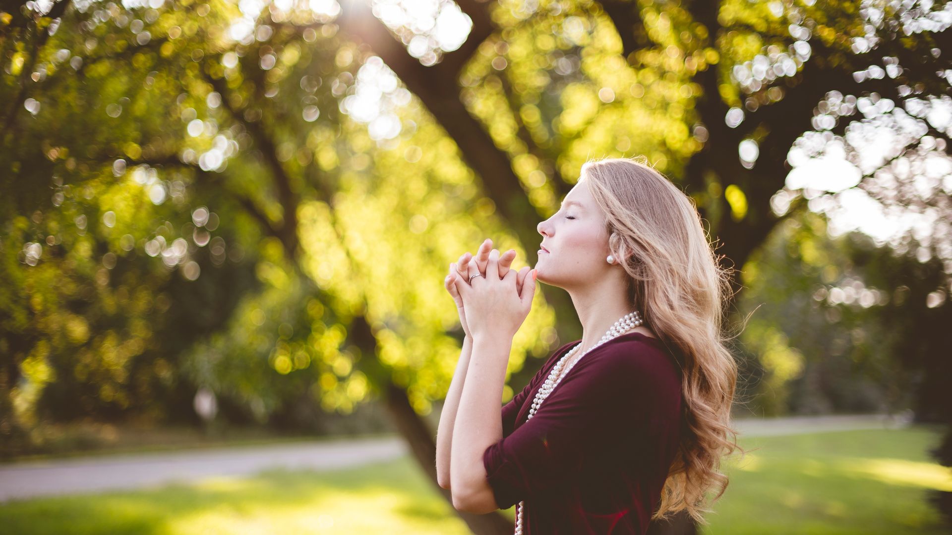 Mulher fazendo oração ao ar livre, com os olhos fechados
