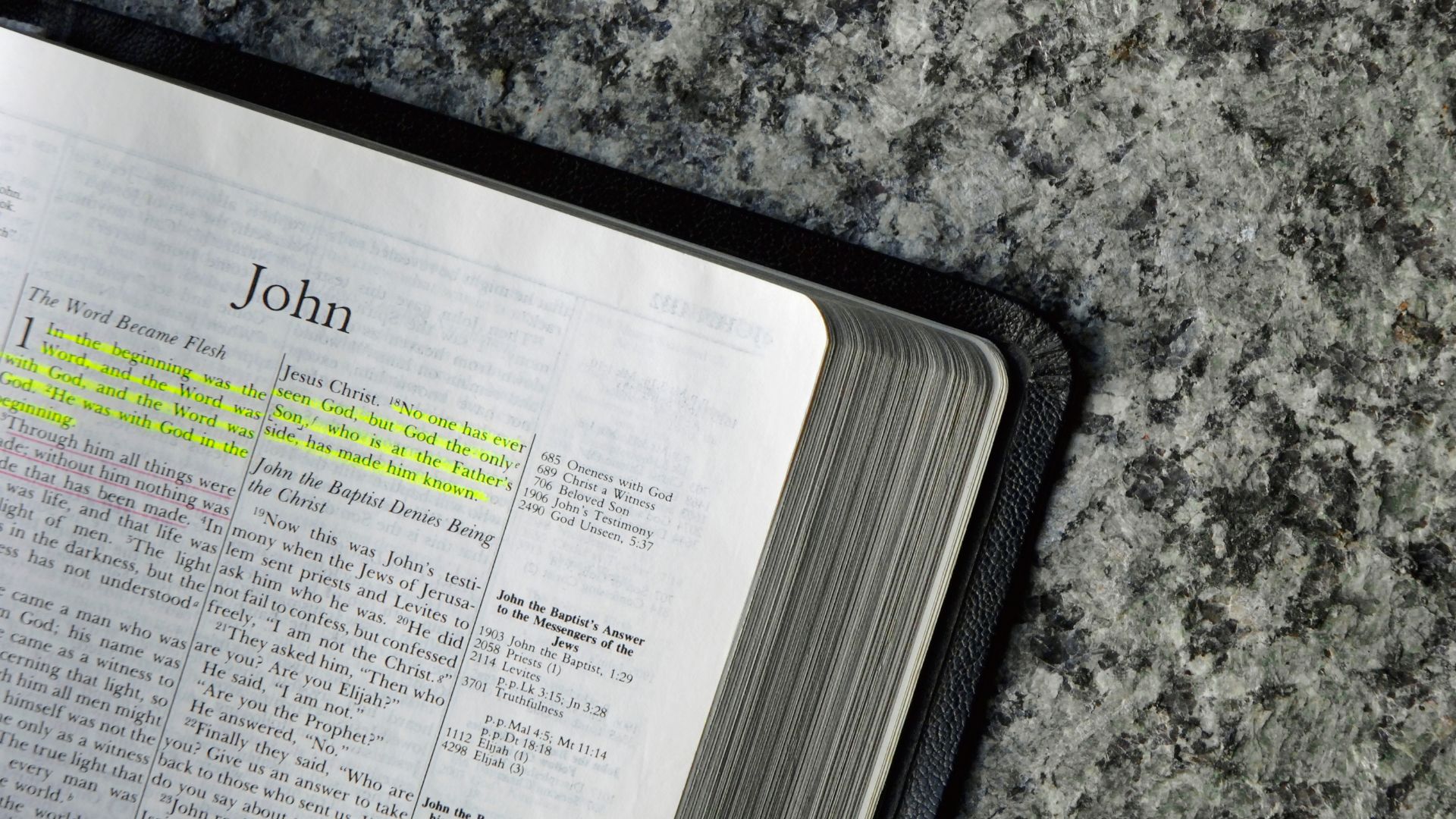 Bíblia aberta com capítulo de João, em mesa de pedra.