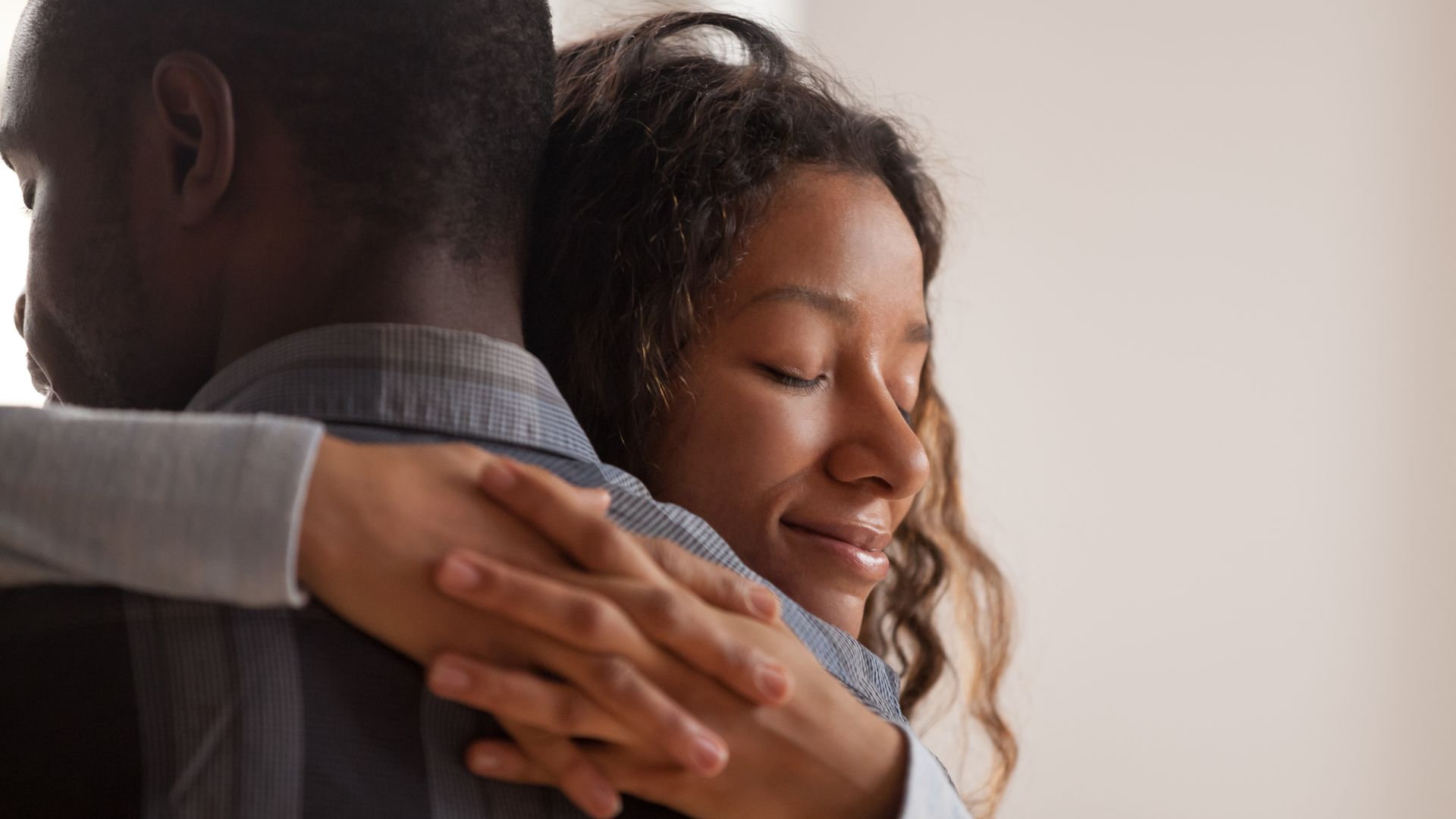 Mulher parda, com os olhos fechados abraçando um homem negro