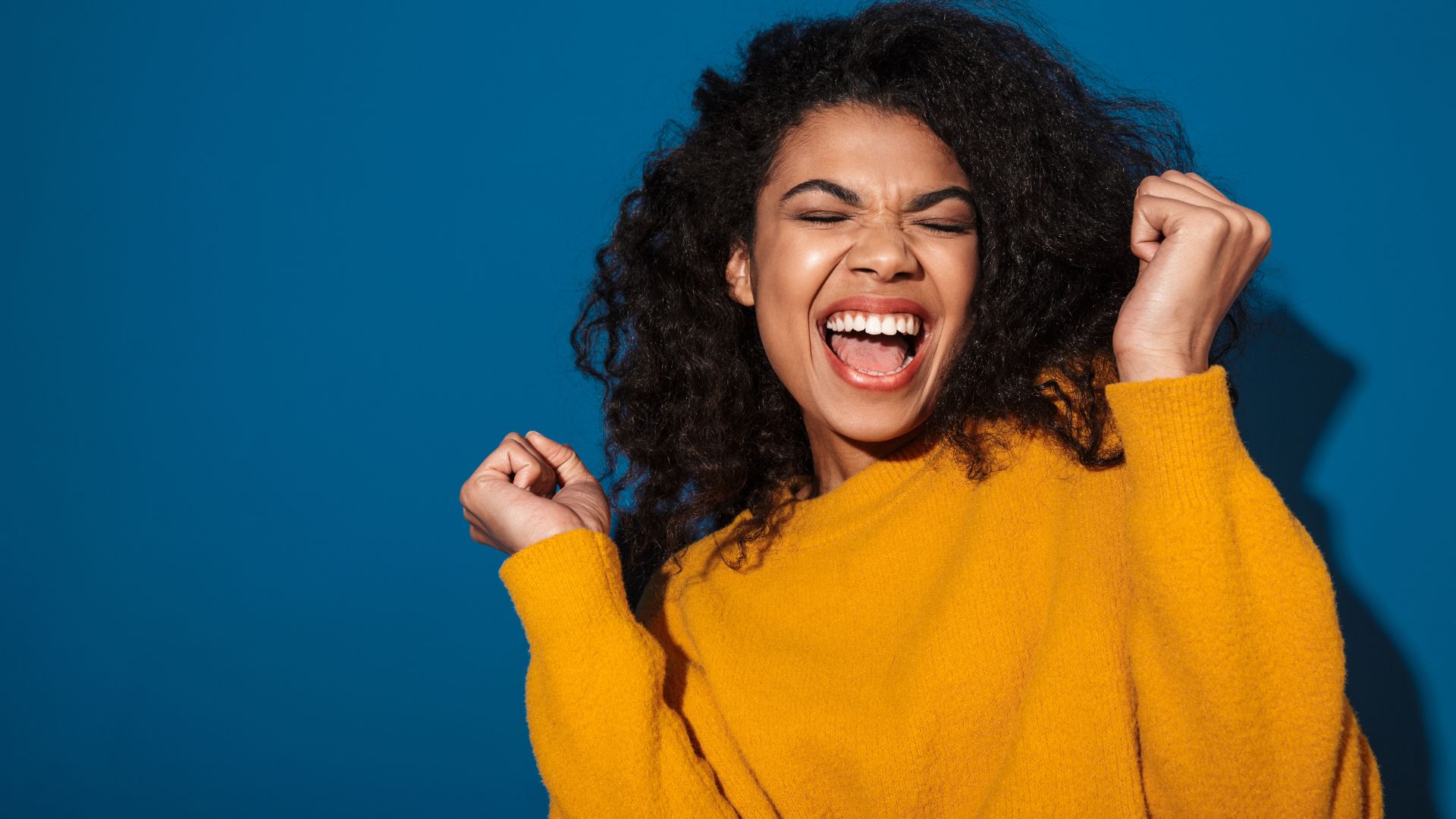 Mulher sorrindo com os olhos fechados e braços erguidos em sinal de comemoração